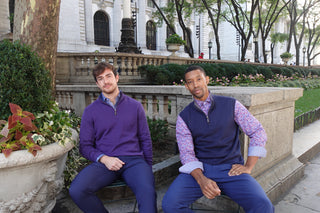 Two men sitting on a bench outdoors with a cityscape background