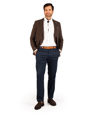 A man modeling a brown blazer, white dress shirt, navy trousers, a brown patterned belt, and brown loafers against a plain white background.