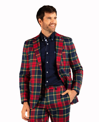 A man wearing a red, navy, and green tartan plaid blazer and matching trousers over a navy blue button-down shirt, photographed against a solid white background.