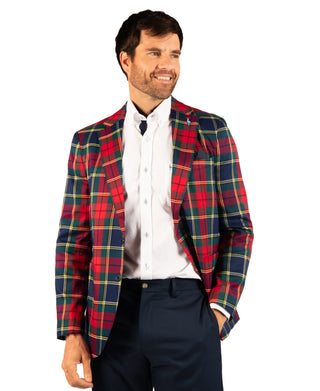 A man wearing a red, navy, and yellow tartan plaid blazer over a white button-down shirt and navy trousers, standing against a plain white background.