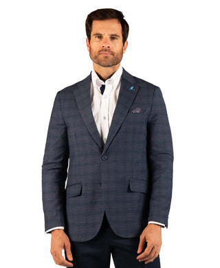 A man wearing a navy blue windowpane plaid blazer over a white shirt and dark trousers, standing against a solid white background.