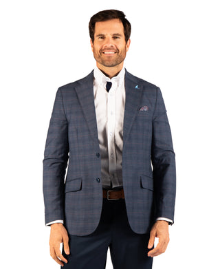 A man wearing a blue and gray plaid suit jacket over a white dress shirt, paired with navy trousers and a brown belt, standing against a solid white background.