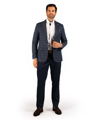 A man modeling a navy blue plaid suit, featuring a blazer and matching trousers, styled with a white dress shirt, a dark tie, and dark brown leather shoes against a plain white background.