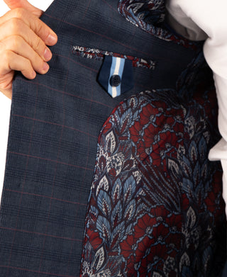Close-up of a person holding open dark navy plaid trousers to show the lining, which features a red, blue, and white floral paisley pattern.
