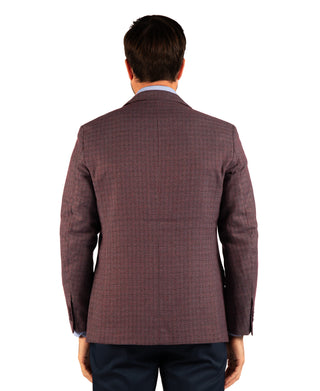 A man viewed from the back wearing a textured, dark reddish-brown plaid blazer over a light blue dress shirt and navy trousers, set against a plain white background.