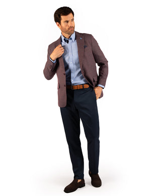 A man modeling a men's blazer in a dusty rose-brown micro-check pattern, paired with a light blue dress shirt, dark navy trousers, a brown belt, and dark brown loafers, set against a plain white background.