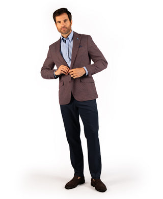 A man modeling a tailored sport coat with a subtle brown and beige check pattern, worn over a light blue dress shirt and dark navy trousers, on a white studio background.