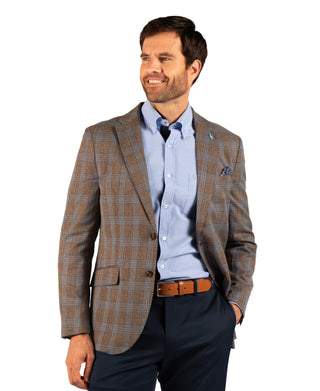 A man wearing a brown and beige plaid blazer over a light blue dress shirt, paired with navy trousers and a brown leather belt, photographed against a solid white background.