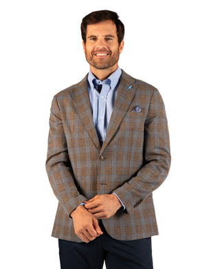 A man wearing a brown and beige plaid blazer over a light blue dress shirt and dark tie, standing against a plain white background.