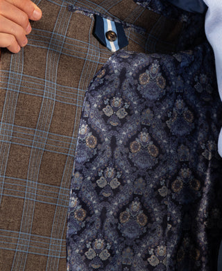 Close-up of a tailored jacket interior and lining: a brown plaid outer fabric, a navy patterned inner lining with floral damask motifs, and a small striped neck label.