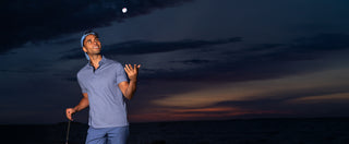 A man in a blue modal polo shirt and matching performance pants throws golf ball up in the air.