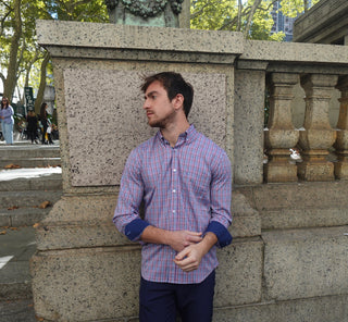 Man in a checkered shirt standing against a stone wall with people in the background