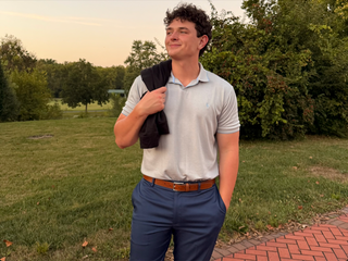 Man holding a black quarterzip outdoors in a park.